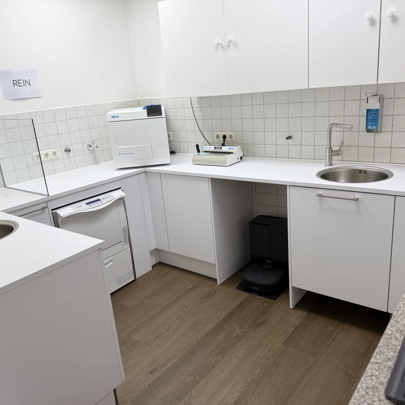 Steriler Raum mit Schränken, Waschbecken und medizinischen Geräten.